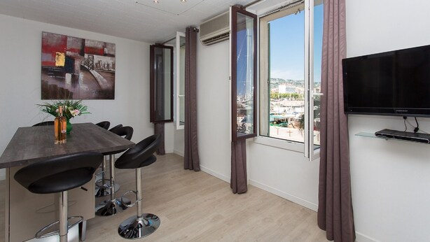 A modern room with a dining area, a TV, and a large window with curtains. - CANNES CENTER, IDEAL CONGRESS, HOLIDAYS, MODERN APARTMENT FACING THE OLD PORT (Cannes)
