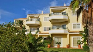 Un edificio de varios pisos con balcones, rodeado de exuberante vegetación y palmeras.