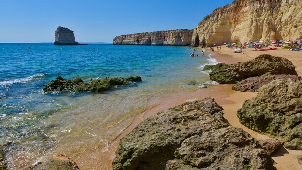Una playa con aguas cristalinas, formaciones rocosas y un acantilado.