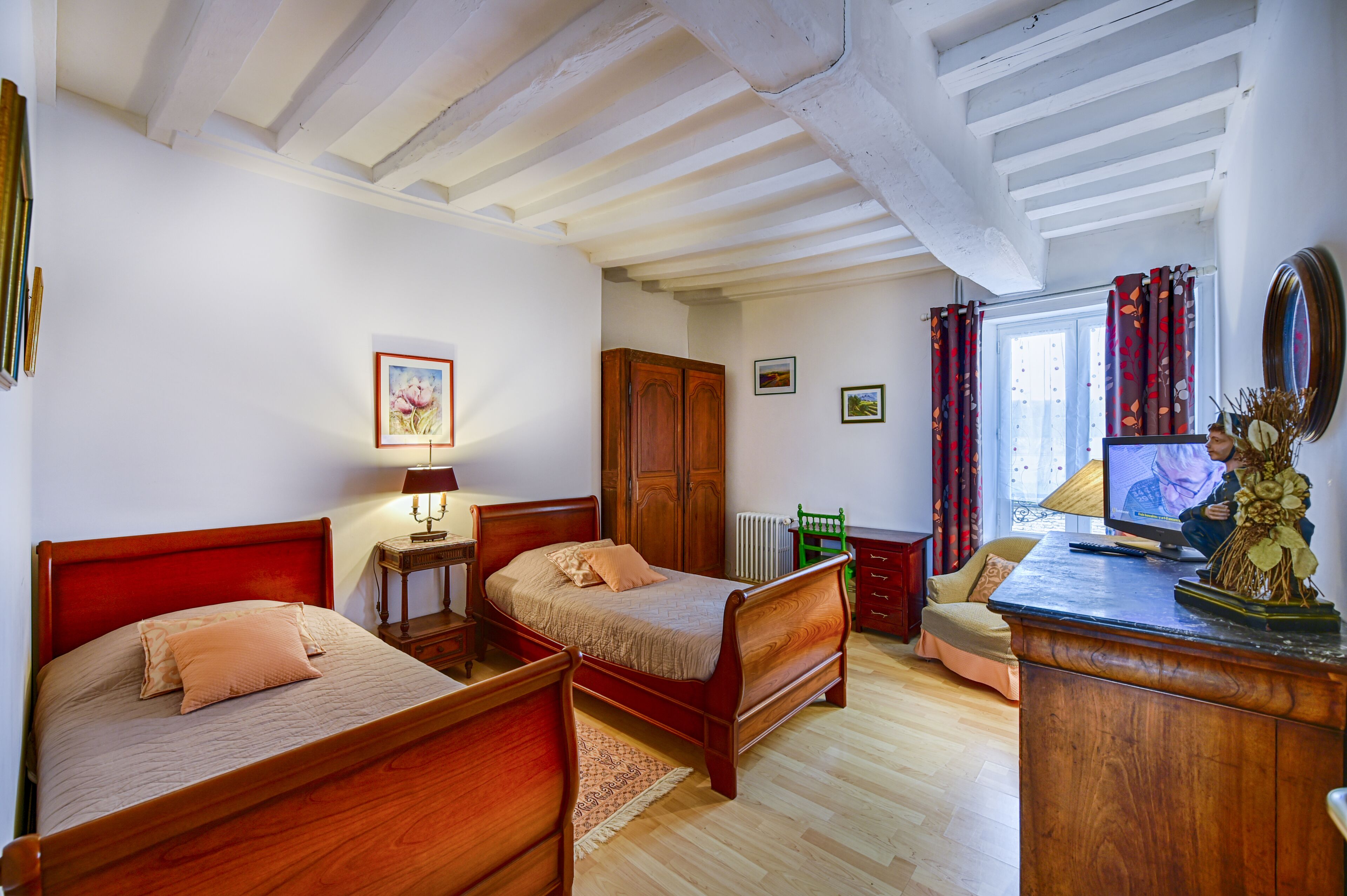 Un dormitorio con dos camas de madera, un aparador de madera, una silla verde y un televisor.