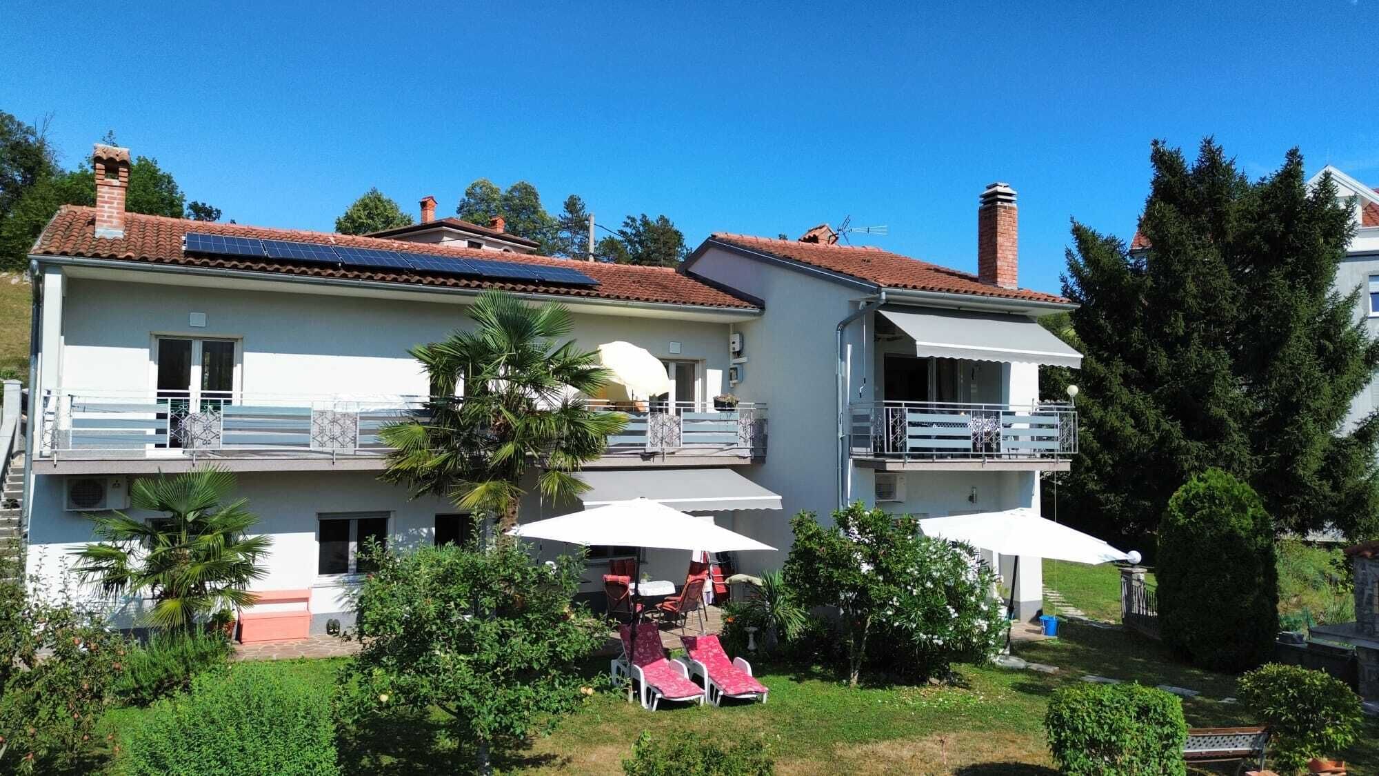A two-story building with a balcony, a pool area with lounge chairs, and a garden.