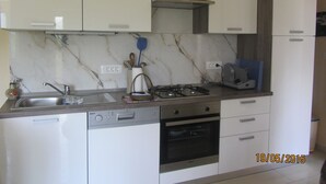Una cocina con armarios blancos, estufa a gas, lavavajillas y microondas.