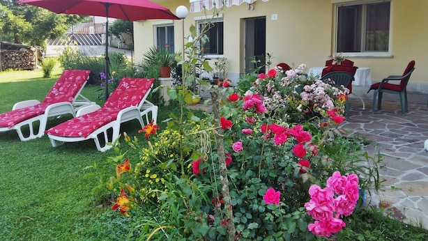 Un patio con sillones de descanso, una sombrilla roja y una gran variedad de flores.