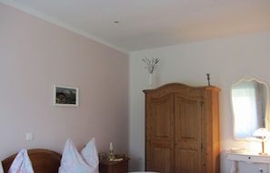 Et soveværelse med et træskab, et natbord med en lampe, et spejl og et billede på væggen.