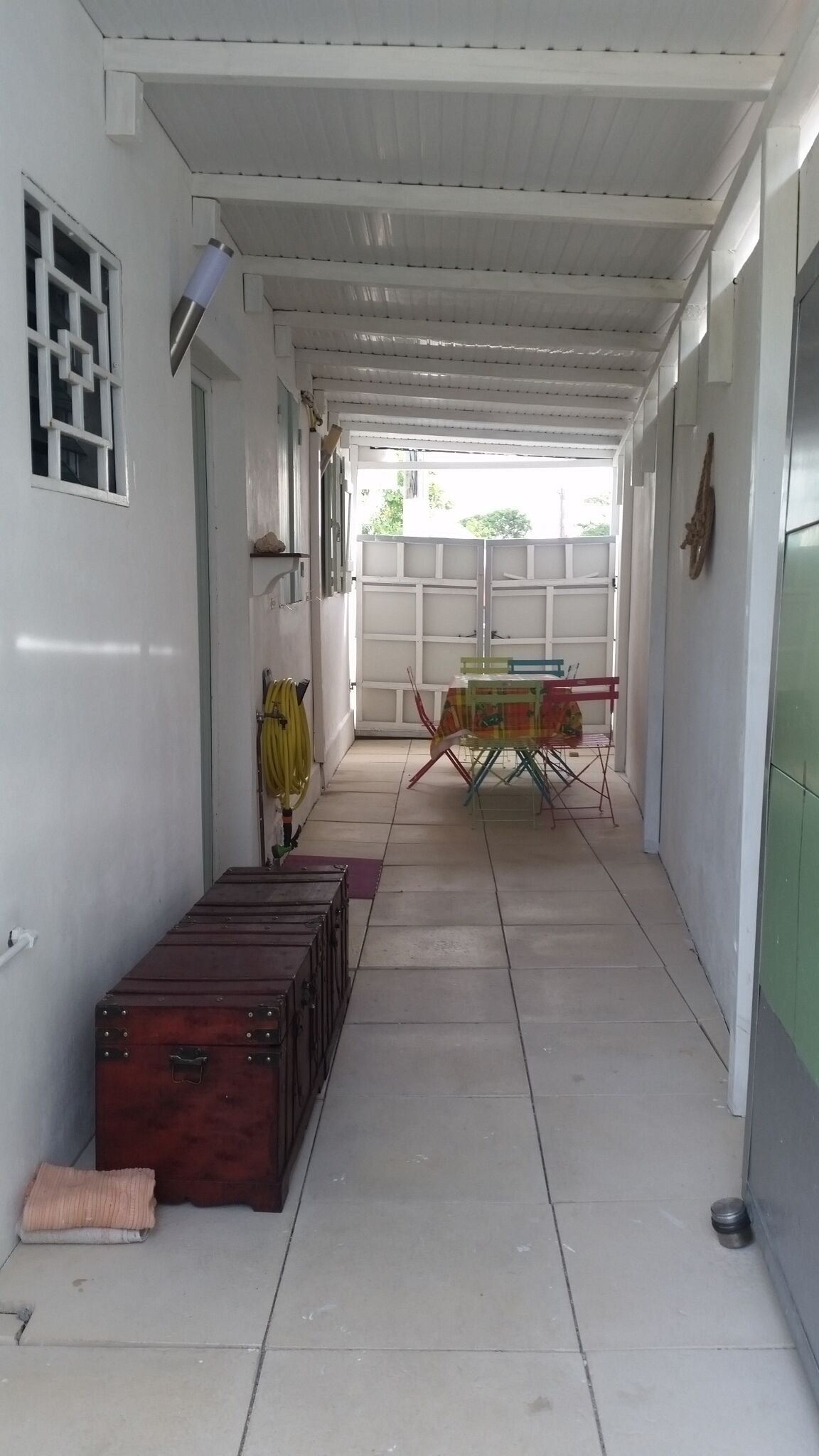 A corridor with a table and chairs, a suitcase, and a window with a geometric pattern.