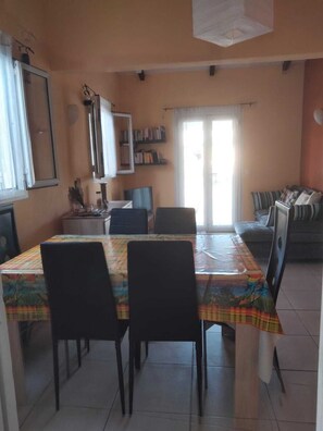 A dining area with a table set for four, chairs, a bookshelf, and a sofa in the background.