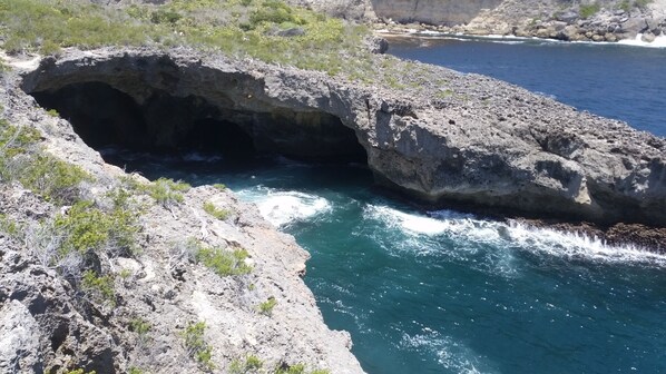 Formación rocosa natural con una abertura similar a una cueva que da a una masa de agua.