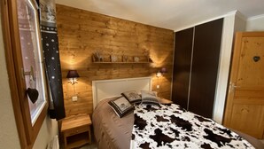 Ein Schlafzimmer mit einem Holz-Kopfteil, einem Bett mit Kuhfellüberzug, Nachttischlampen, einem kleinen Nachttisch aus Holz und einem Regal mit Dekoration.