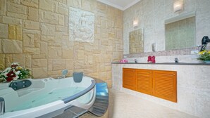 A bathroom with a stone wall, a large bathtub, a wooden vanity, and a mirror. - Luxurious, quiet, private Pool-Villa Jasmine, 7/7 housekeeper/butler (Phuket)