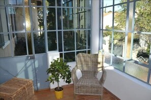 Relax in a serene space with a large window offering views of the surrounding area, a wicker chair, and a small table.