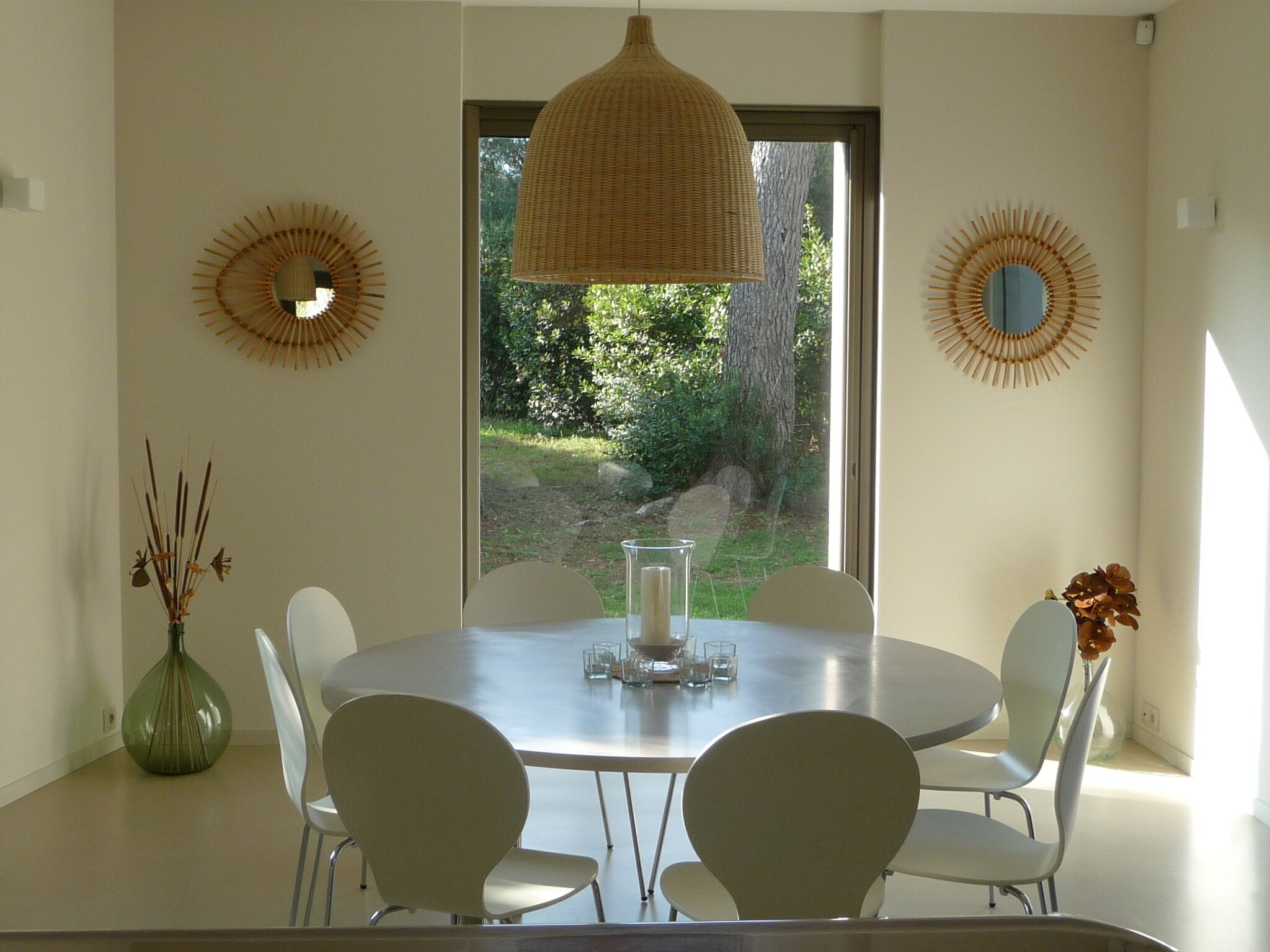 A dining area with a round table, white chairs, and a hanging light fixture.