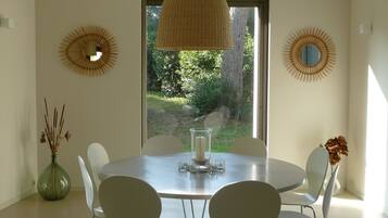 A dining area with a round table, white chairs, and a hanging light fixture.