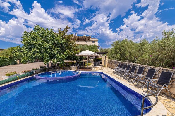 A swimming pool with a stone deck, lounge chairs, and a gazebo.