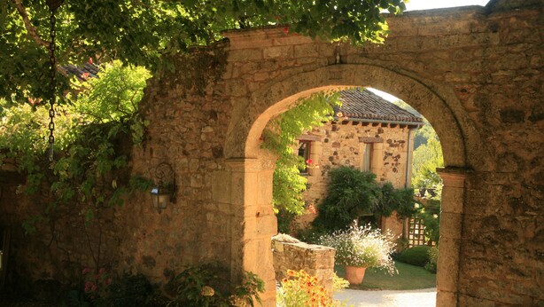 An arched stone gateway leading to a building with a tiled roof, surrounded by lush greenery and potted plants. - -Domaine de Cournet Haut-Le Saule: featuring a pool, tennis court, and bicycles on 5 hectares (Saint-Pompont)