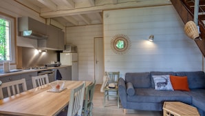 A modern kitchen with white cabinets, a wooden dining table, and a gray sofa with decorative pillows. - Vacation rental in self-catering village with heated swimming pool near Sarlat (Orliaguet)