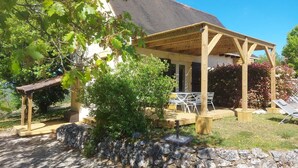 A covered outdoor seating area with stone walls, a wooden pergola, and a view of a house with a tiled roof. - Vacation rental in self-catering village with heated swimming pool near Sarlat (Orliaguet)
