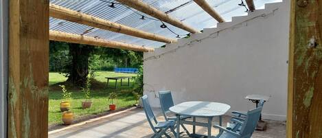 Eine überdachte Terrasse mit Tisch und Stühlen, ein überdachter Pergola und Blick auf eine grüne Landschaft.