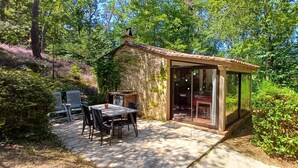 Un petit bâtiment en pierre avec un toit en tuiles, une porte en verre et une terrasse avec une table et des chaises.