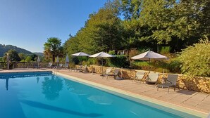 Une piscine entourée de murs de pierre et de verdure, avec des chaises longues et des parasols.