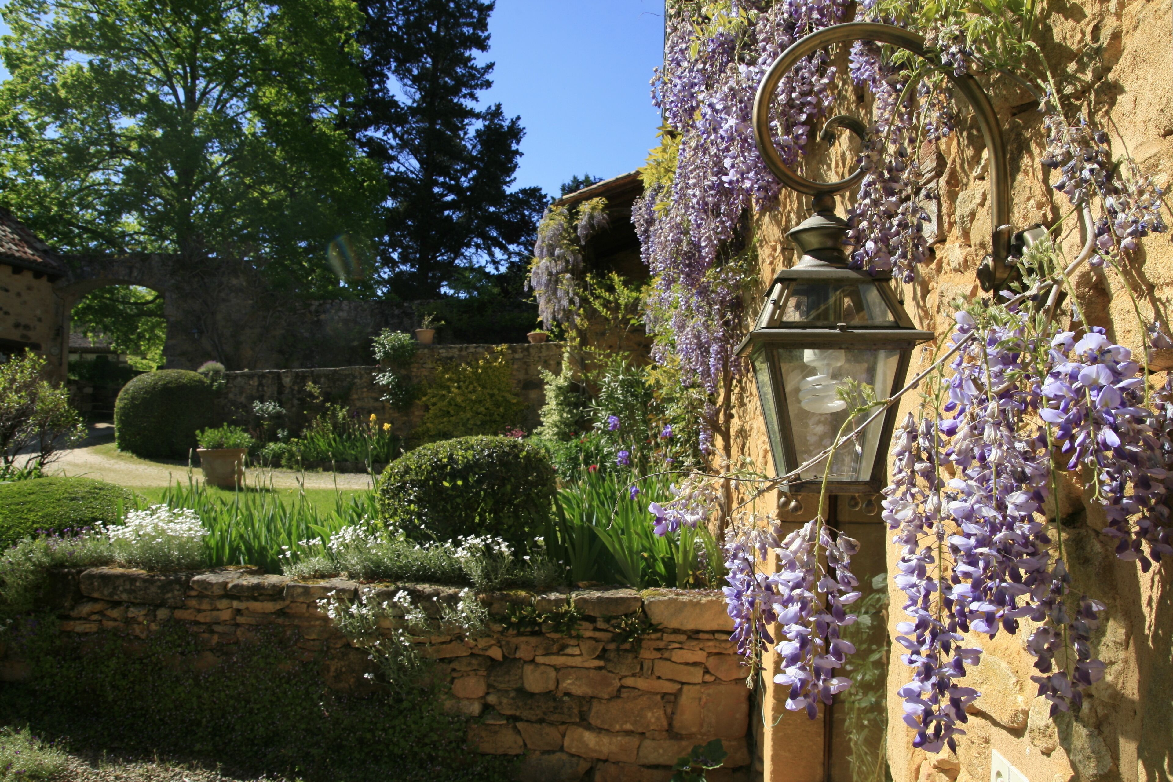 Eine Steinsäule mit einem hängenden, violetten Blumenarrangement und einer Laterne.