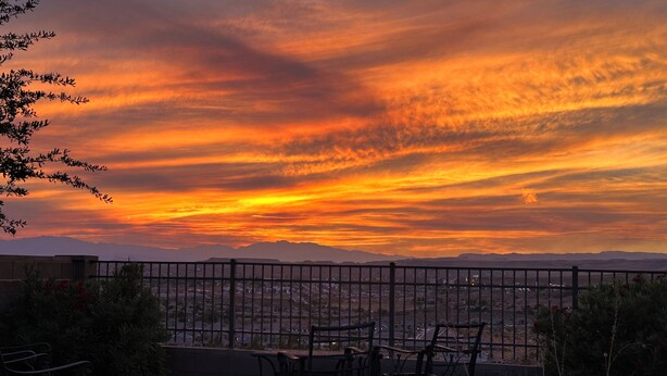 A sunset view from a balcony with a metal railing, featuring a patio with chairs and a stone pathway. -  CORAL CANYON VIEW HOME !!!! UP ON THE LEDGE! DOG FRIENDLY! (Washington City)