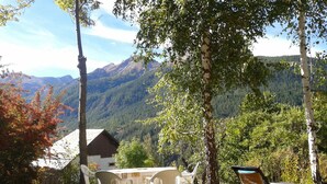 Mesa con sillas y una mesa de comedor al aire libre, rodeada de árboles y con vistas a montañas.