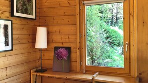A wooden cabin interior with a window overlooking a forest, a desk with a lamp, and framed pictures on the wall. - Châlet located in PLAGNE Centre, rated 4 Paradiski crystals and furnished for tourism, (La Plagne Tarentaise)