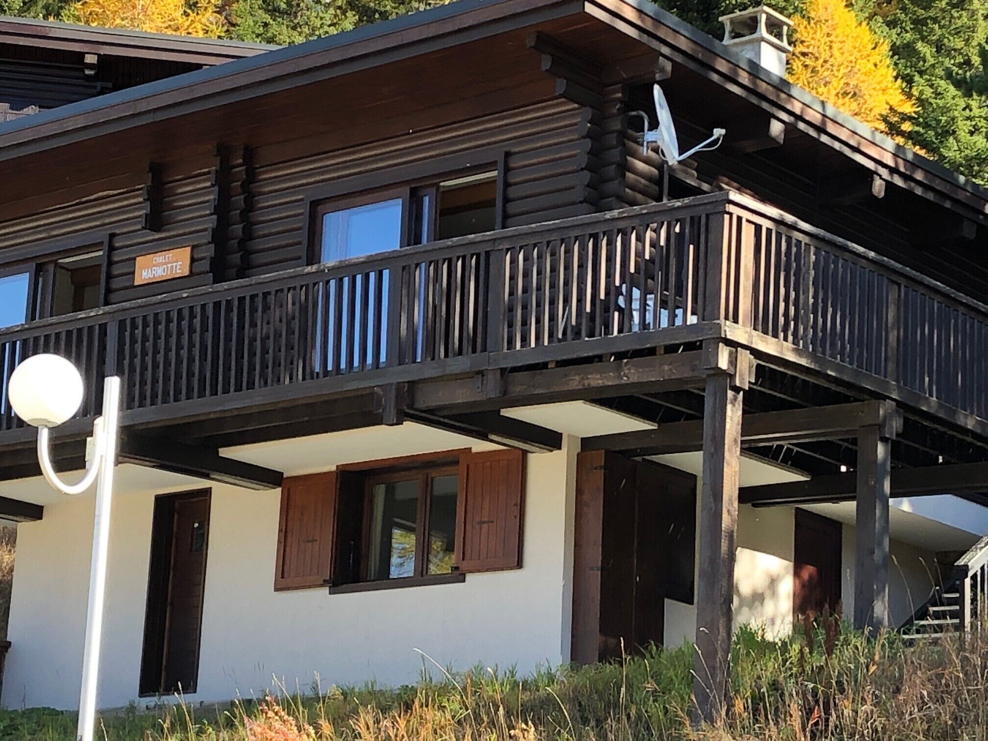 A two-story log cabin with a balcony, a satellite dish, and a sign that reads "Chalet Marmotte".