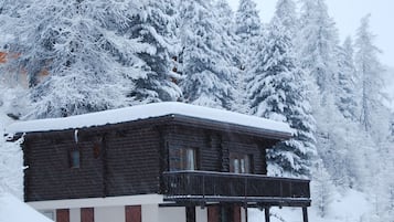 Une cabane en rondins dotée d’un balcon, entourée d’arbres couverts de neige.