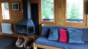A cozy cabin interior with a wooden interior, a fireplace, a sofa with cushions, and windows overlooking a forest. - Châlet located in PLAGNE Centre, rated 4 Paradiski crystals and furnished for tourism, (La Plagne Tarentaise)