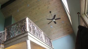 Une pièce aux hauts plafonds, avec un plafond en bois, un balcon doté d’une balustrade ouvragée et un ventilateur de plafond.