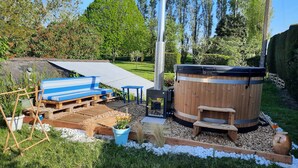Een hottub met een houten buitenkant, een blauwe bank en een tafel in een tuin.