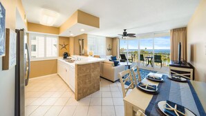 A modern kitchen with a central island, a dining area with a view, and a balcony with a view of the ocean.