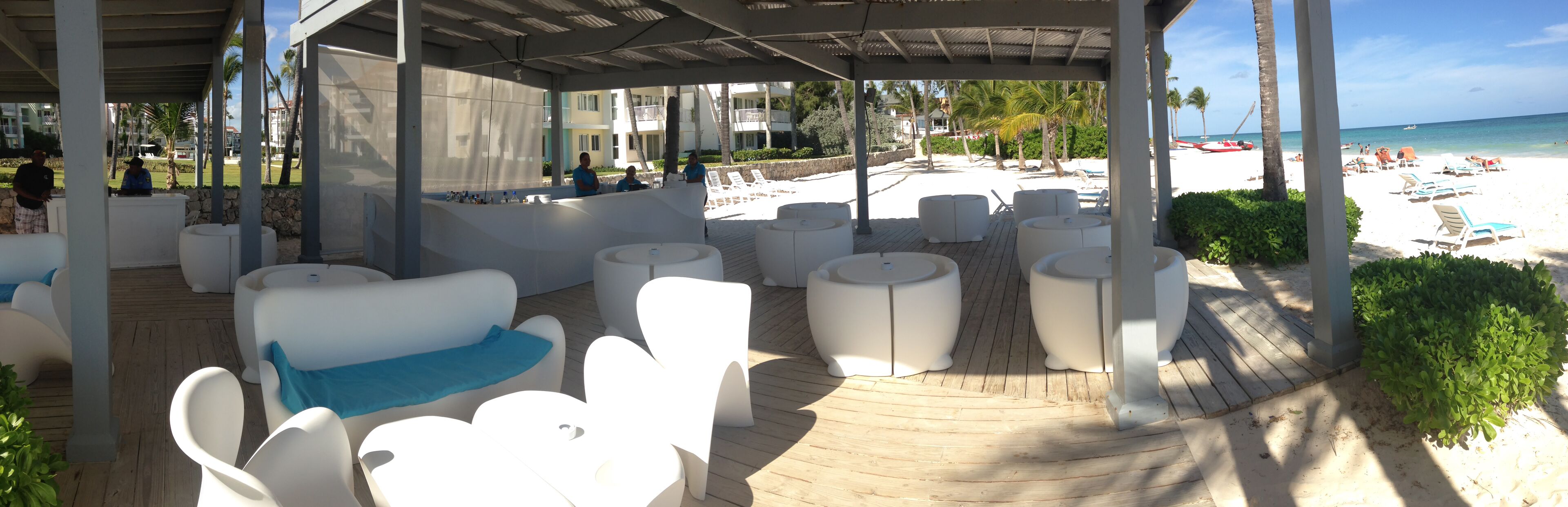 A covered outdoor seating area with white furniture and a view of the beach.