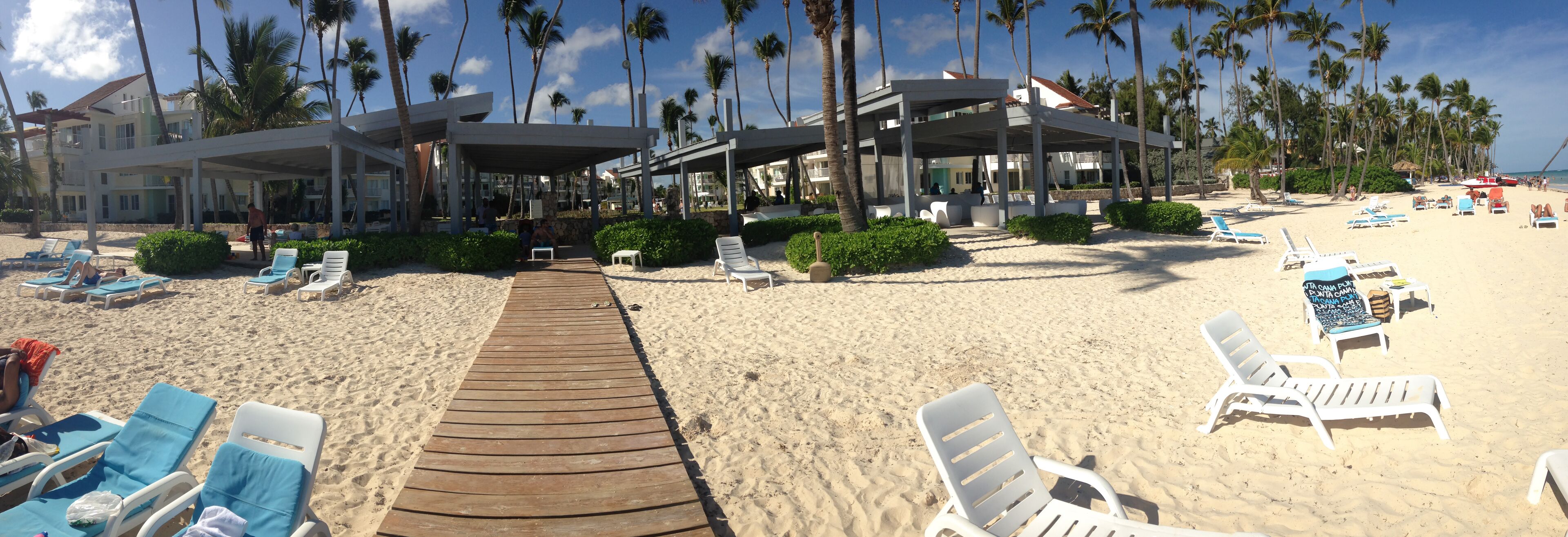 A beach with a wooden walkway leading to a covered area with lounge chairs and umbrellas.