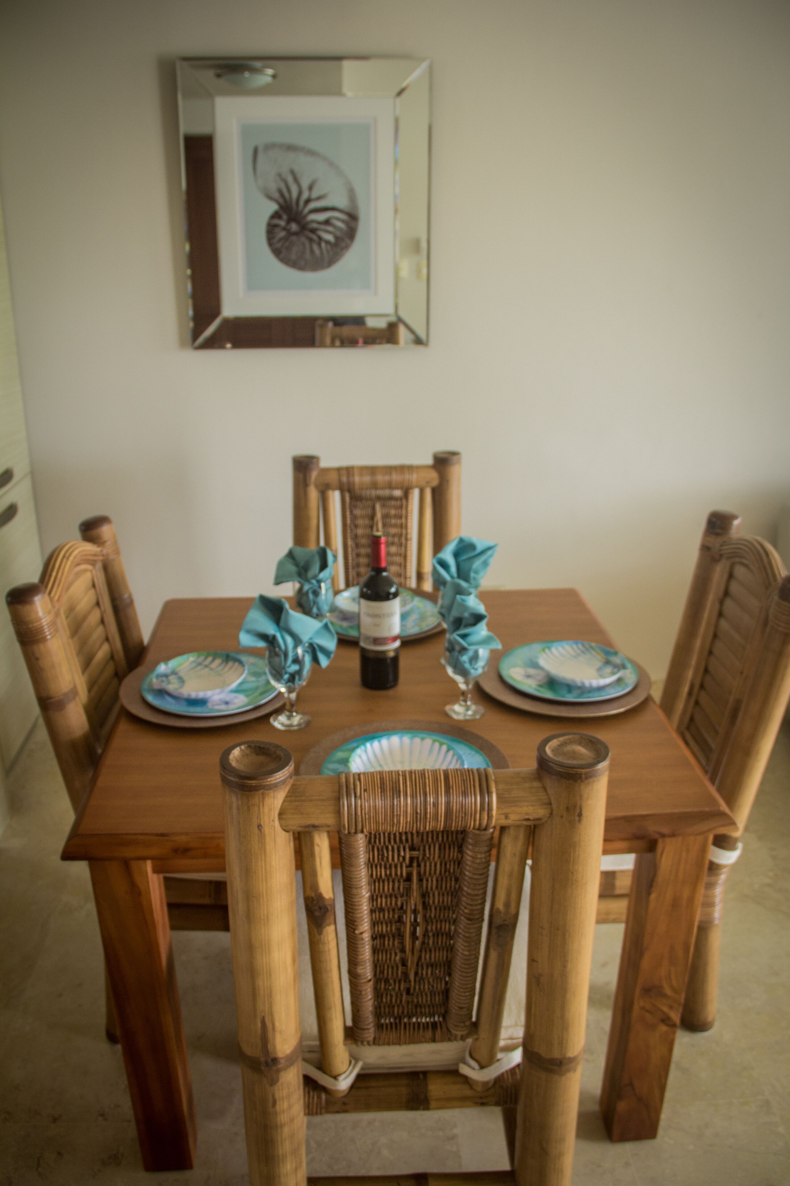 Une table à manger avec quatre chaises, un tableau encadré au mur et une bouteille de vin.