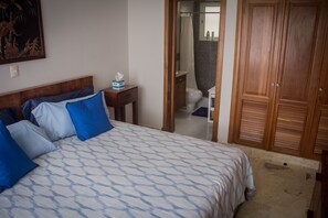Een slaapkamer met een bed, een nachtkastje, een houten garderobe en een badkamer die door een open deur zichtbaar is.