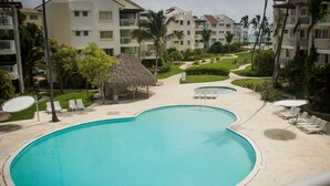 Una piscina dalla forma particolare, circondata da sdraio e una struttura con tetto di paglia.