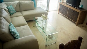 Un soggiorno con un divano beige, un tavolino in vetro, un mobile in legno con televisore e vista panoramica attraverso una porta vetrata.