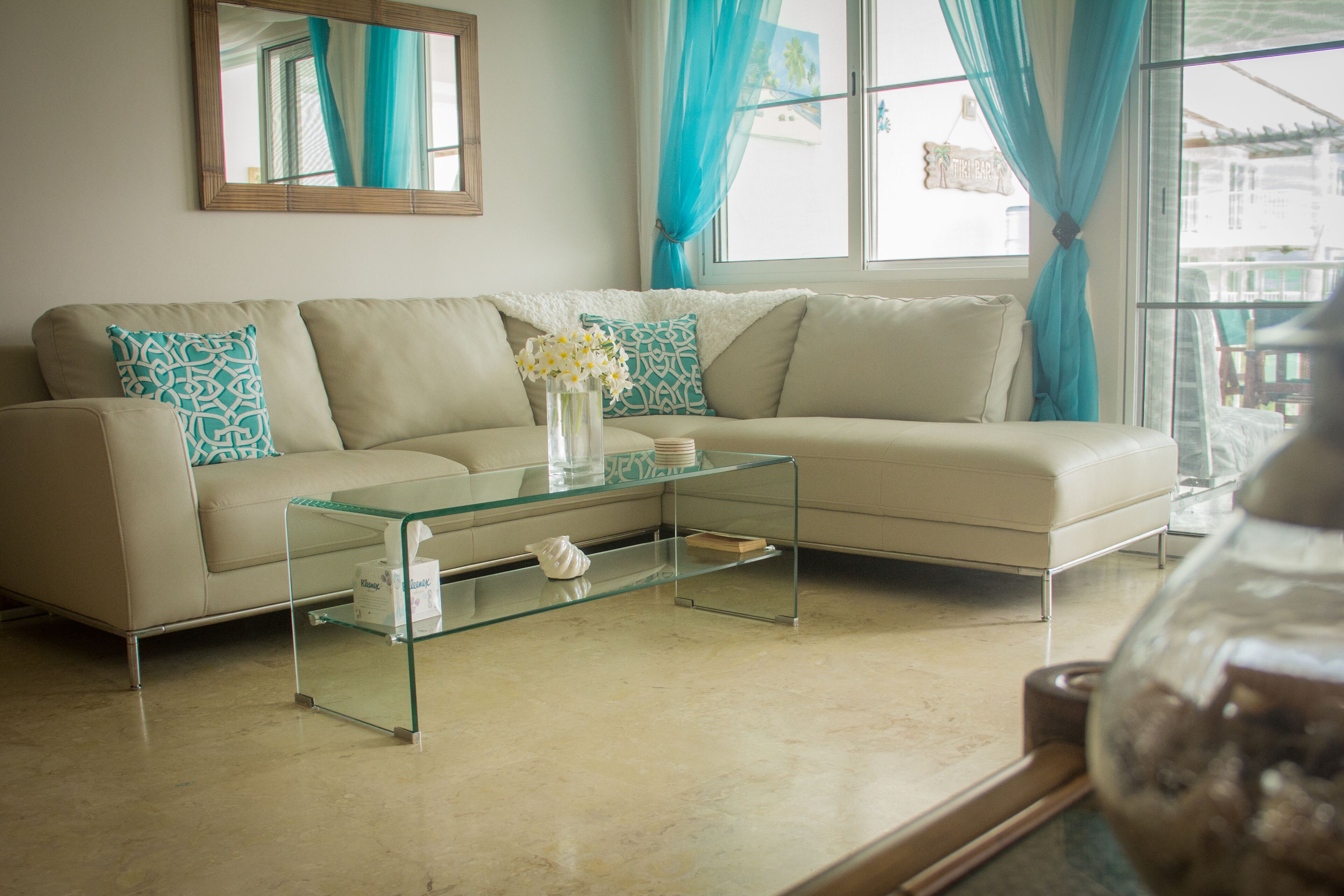 A living room with a beige sofa, a glass coffee table, and a vase with flowers.