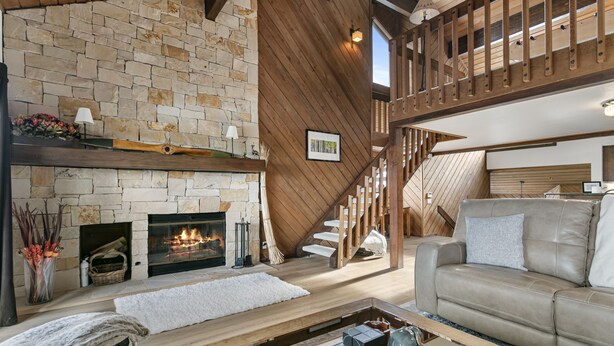 A cozy living room with a stone fireplace, a wooden staircase, and a comfortable sofa.