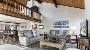 A spacious living room with a high ceiling, a wooden staircase, and a dining area.