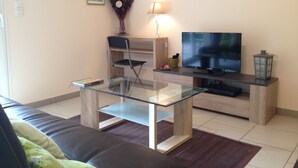 A modern living room with a glass coffee table, a dark leather sofa, a wooden TV stand, and a flat-screen TV. - COTTAGE IN THE HEART OF THE COUNTRY CATHAR (Fanjeaux)
