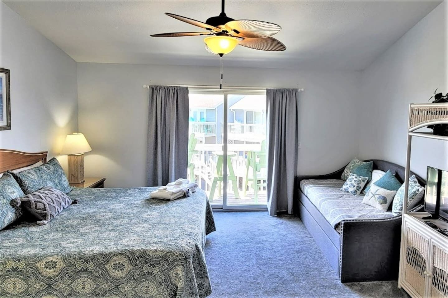 Habitación de hotel con cama, sofá, ventilador de techo, ventana con cortinas y vistas a edificios.
