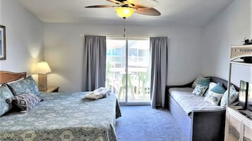 Habitación de hotel con cama, sofá, ventilador de techo, ventana con cortinas y vistas a edificios.