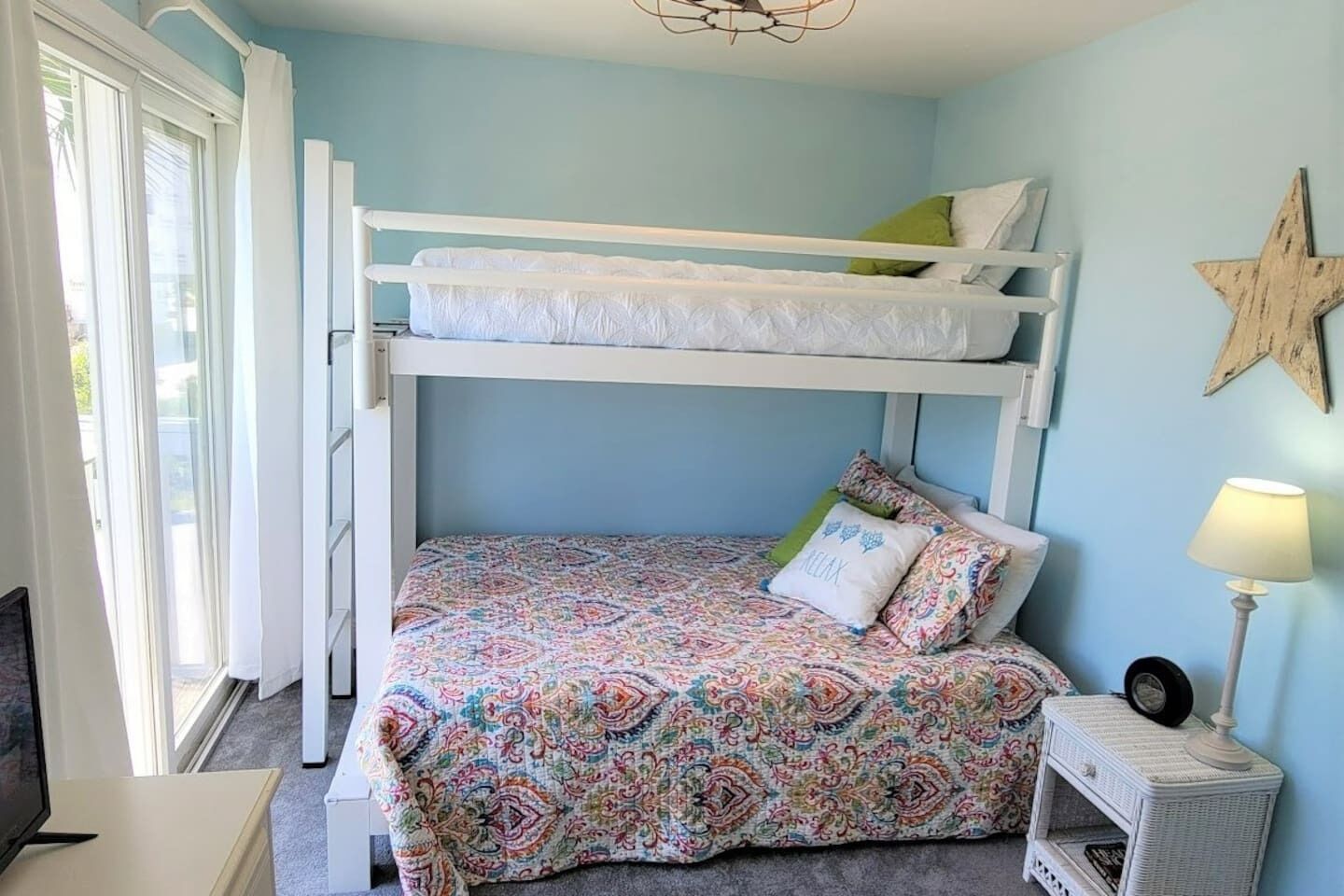 A bunk bed room with a patterned bedspread, a star decoration on the wall, and a bedside lamp.