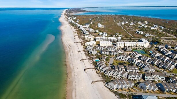 An aerial view of a coastal residential area with beachfront properties, a large hotel complex, and a clear view of the ocean.
