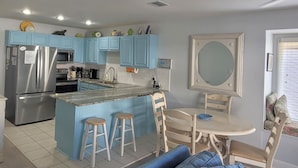A kitchen with blue cabinets, a stainless steel refrigerator, a microwave, and a sink. There is a dining area with a table and chairs.