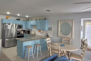 A kitchen with blue cabinets, a stainless steel refrigerator, a microwave, and a sink. There is a dining area with a table and chairs.