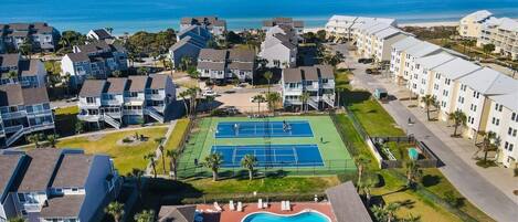 A residential area with a tennis court, pool, and beachfront view.